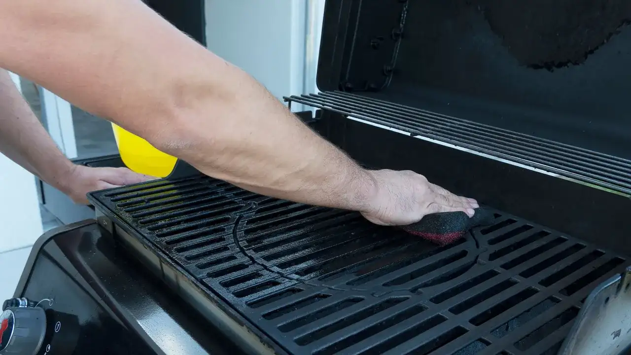 Uomo pulisce la griglia della barbecue con una spugna. Un liquido giallo viene versato da un contenitore.