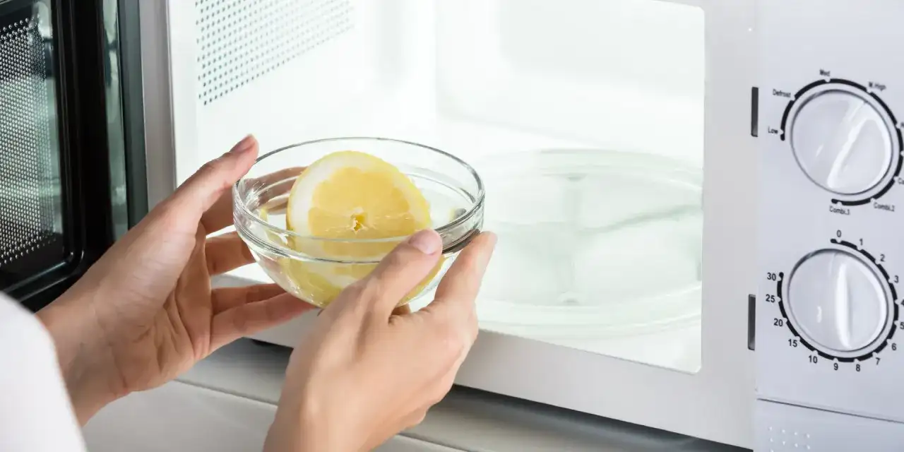 Mani inseriscono una ciotola con acqua e limone nel microonde, un metodo semplice per pulire l'elettrodomestico.