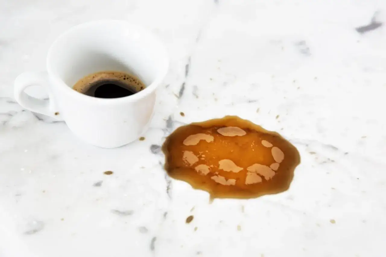Tazza di caffè rovesciata su un pavimento in marmo bianco, creando una macchia scura. Urgente pulire pavimento marmo molto sporco.