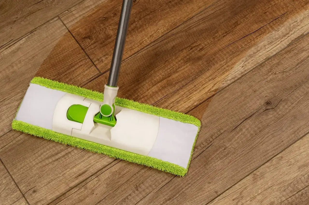 Un mocio con panno verde e bianco pulisce un pavimento in legno, mostrando come sgrassare il pavimento con efficacia.