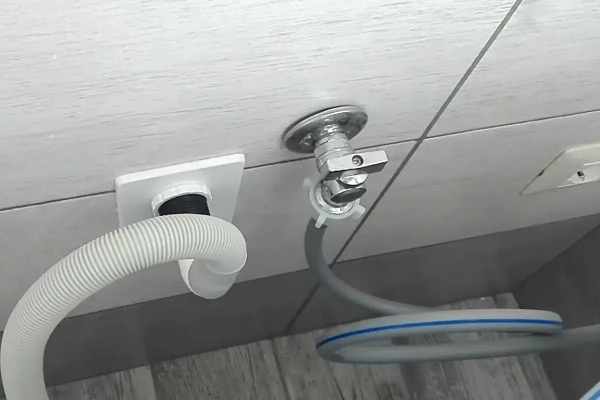 Connessioni idrauliche per lavatrice: tubo di scarico bianco e tubo di carico grigio collegato al rubinetto.