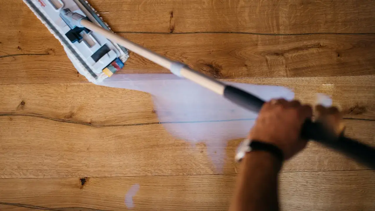 Mano che pulisce il parquet con uno straccio, rimuovendo le strisciate delle scarpe.
