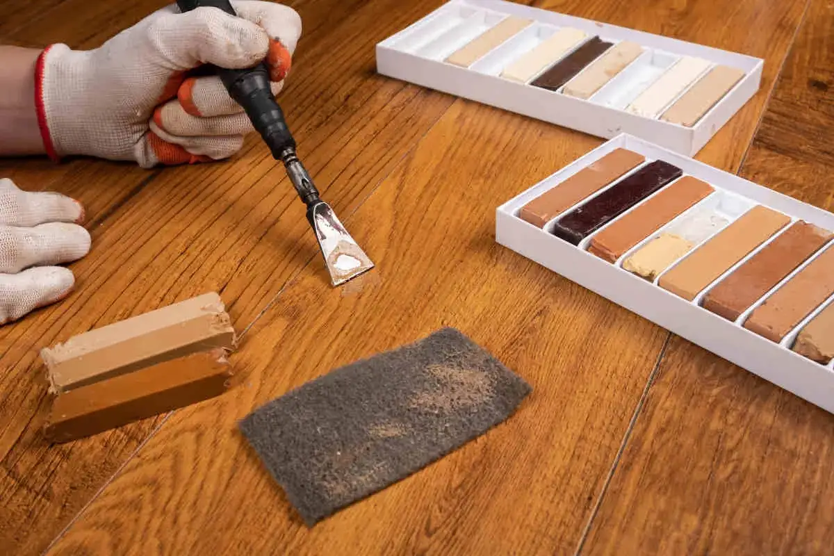 Kit per rimuovere la cera dal parquet verniciato: spatola, tamponi abrasivi e bastoncini di cera colorata per riparazioni.