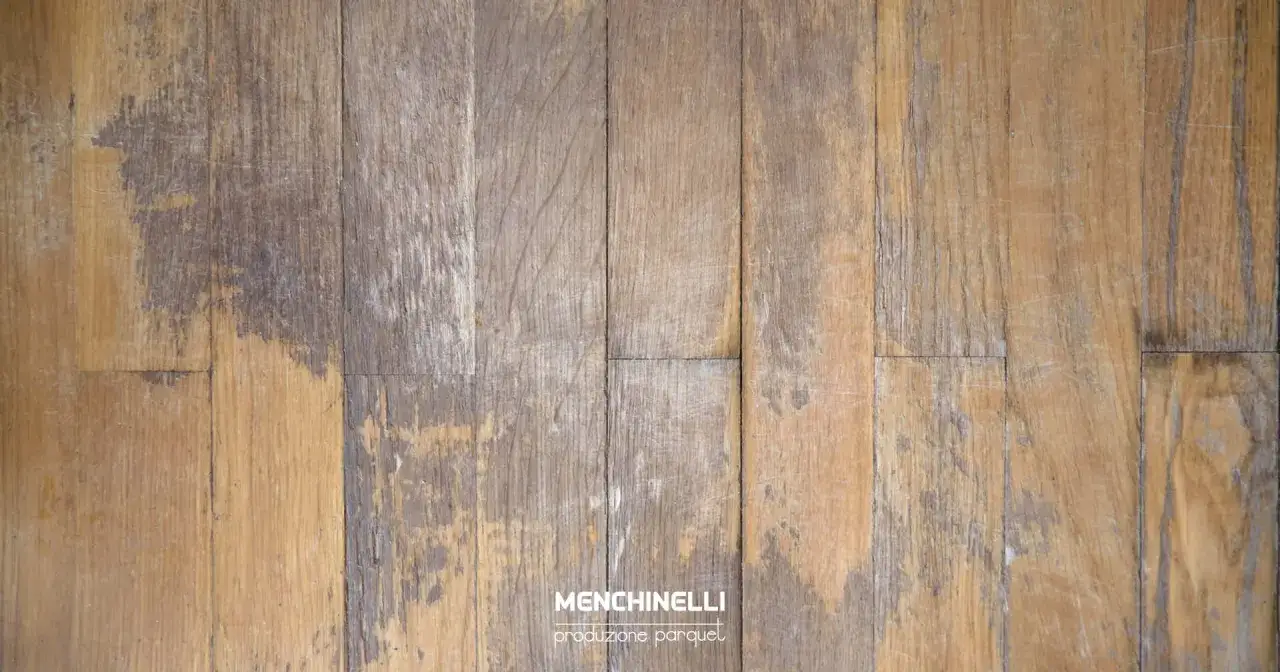 Parquet rovinato con segni di usura e macchie scure, pronto per essere riportato al suo antico splendore.