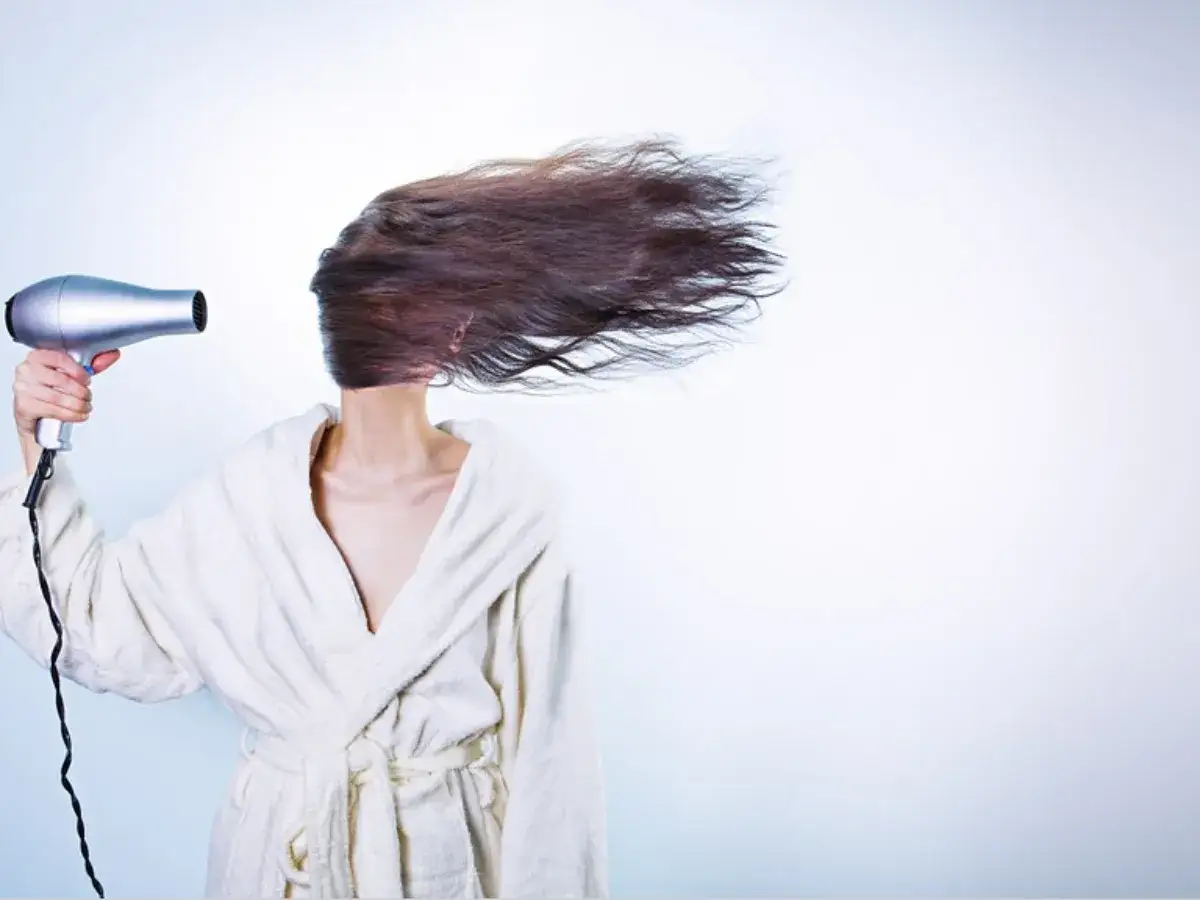 Persona con capelli secchi e sfibrati, asciugati con un phon che li fa volare.