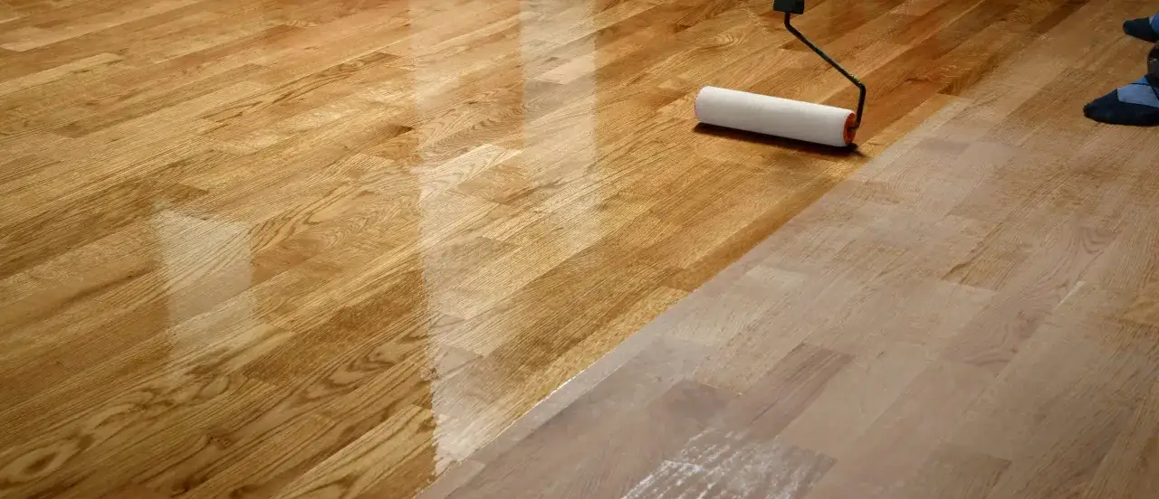 Rullo applica verniciatura parquet su legno chiaro, creando una finitura lucida e protettiva.