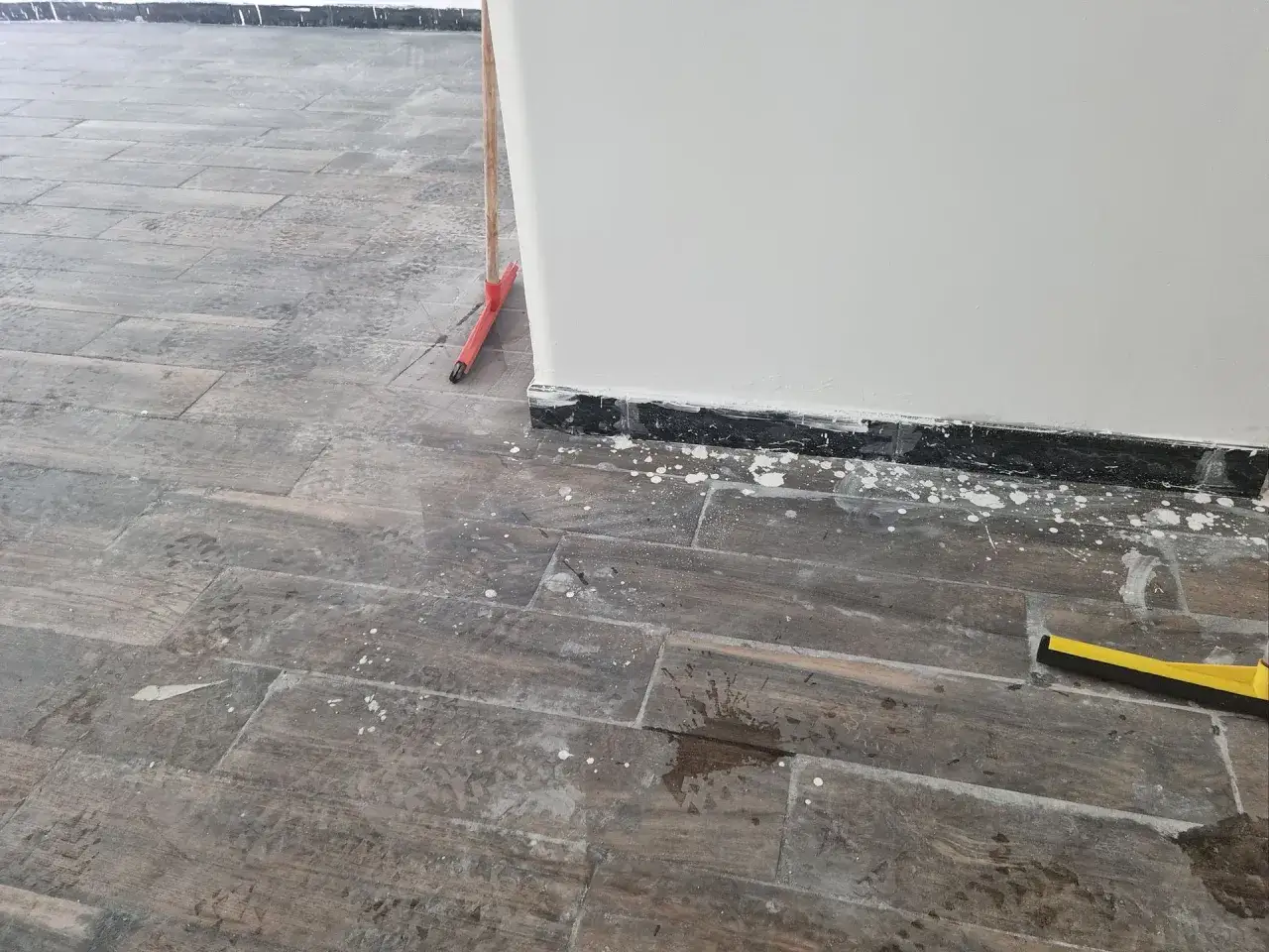 Spruzzi di vernice sul pavimento in legno. Un manico rosso spunta dall'angolo, pronto per pulire.