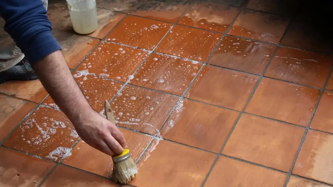 Mano che pulisce con una spazzola un tappeto su pavimento cotto con schiuma.