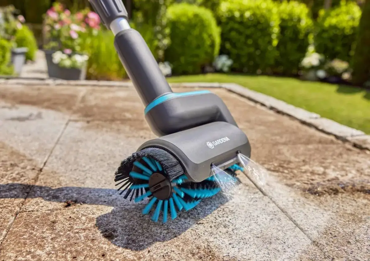 Spazzola elettrica in azione per pulire cemento con candeggina, rimuovendo sporco e muschio dal vialetto del giardino.