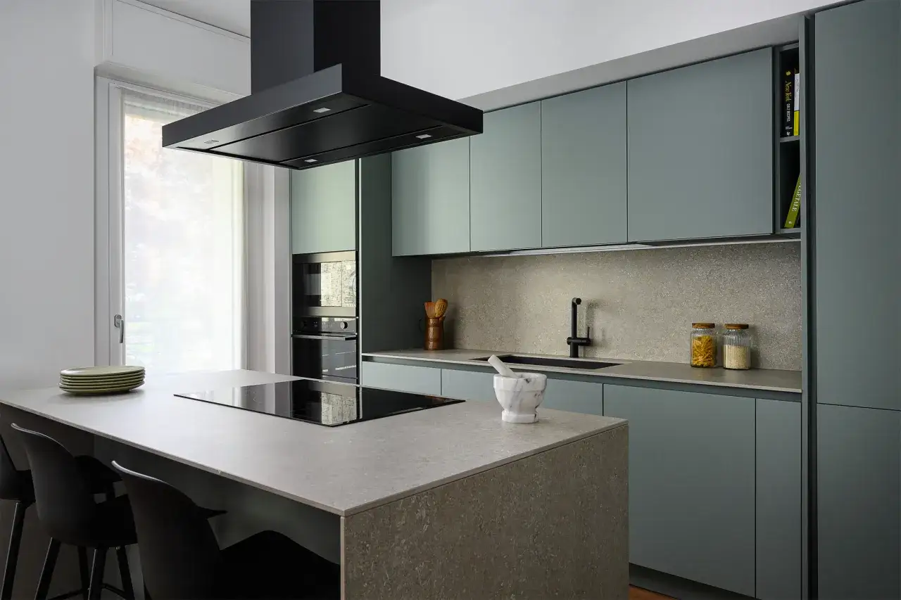 Cucina moderna con isola centrale e piano in ardesia. Ante color salvia, cappa nera e dettagli eleganti.