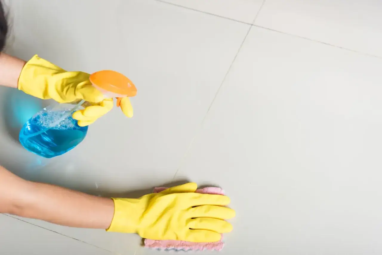Mani con guanti gialli spruzzano detersivo pavimenti fai da te e puliscono con un panno.