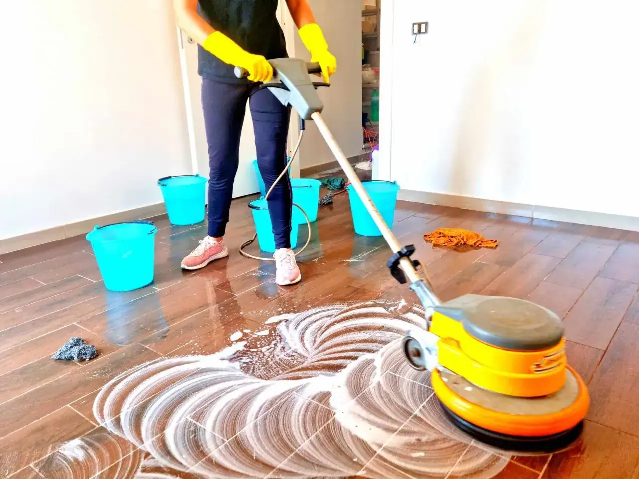 Persona con guanti gialli usa una lucidatrice per pavimenti per pulire la fuliggine dal pavimento in legno.