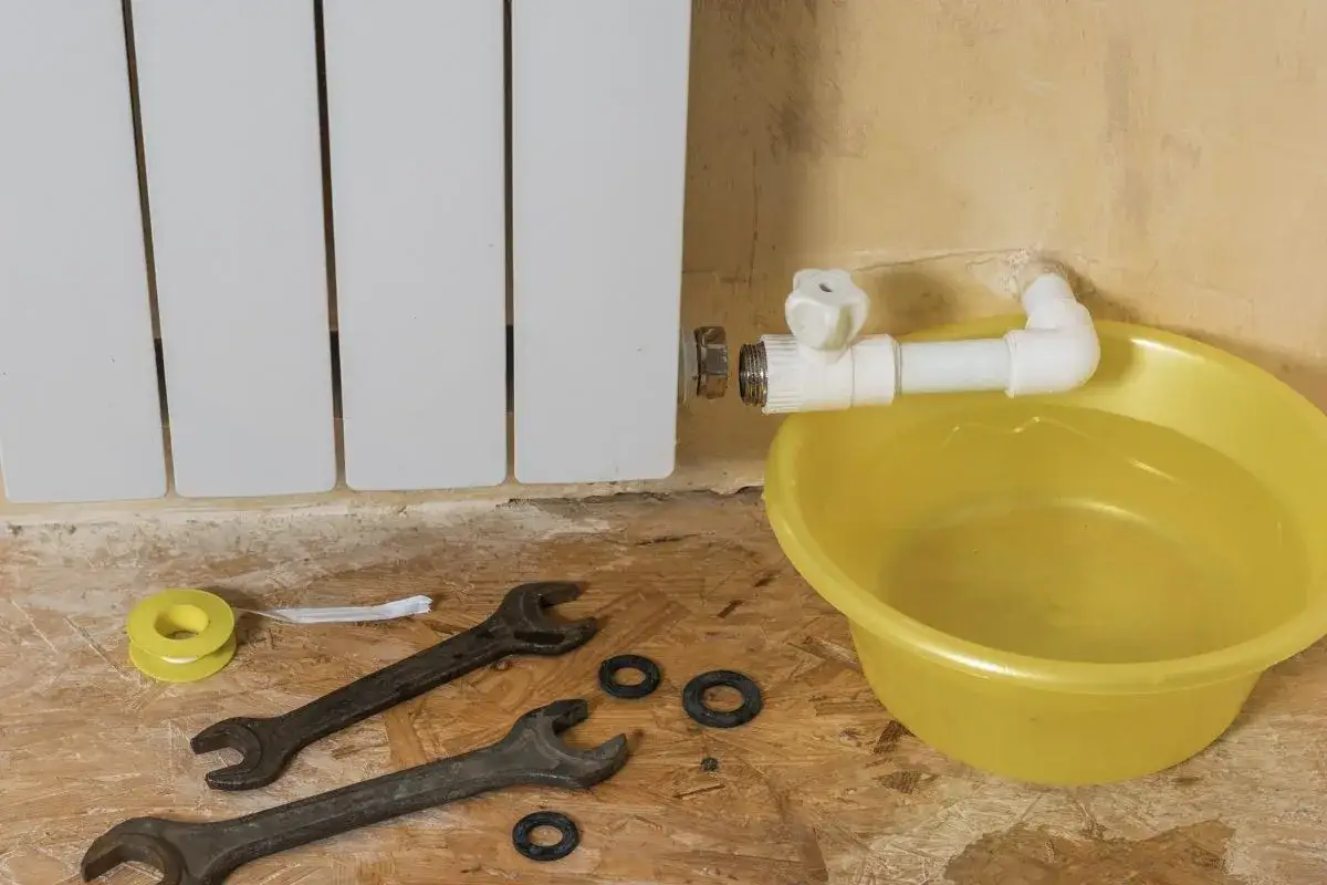 Un termosifone bucato perde acqua. Attrezzi e una bacinella gialla piena d'acqua sono pronti per la riparazione.