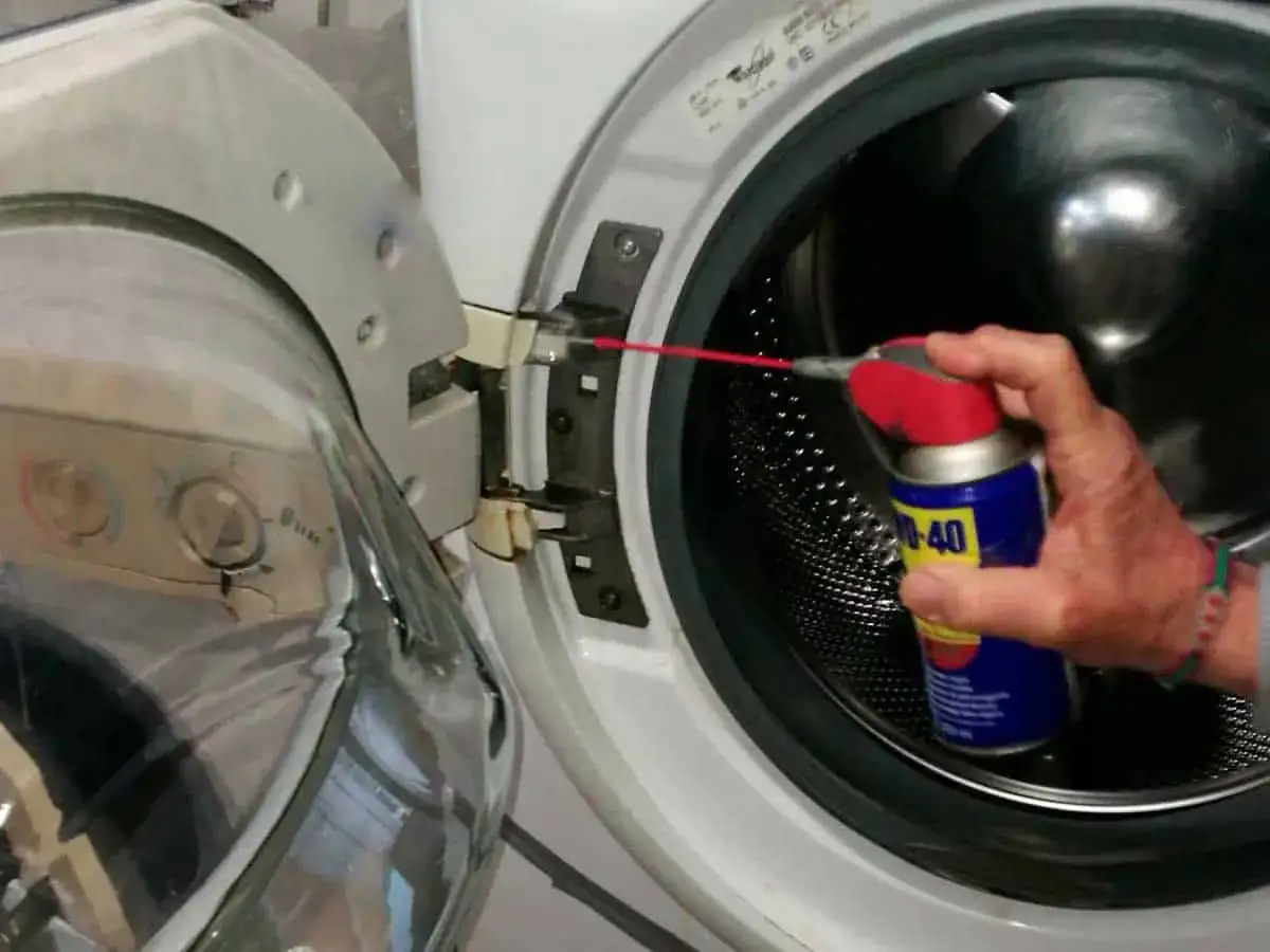 Mano spruzza WD-40 sulle cerniere della lavatrice per lubrificare e facilitare la pulizia dell'oblò.