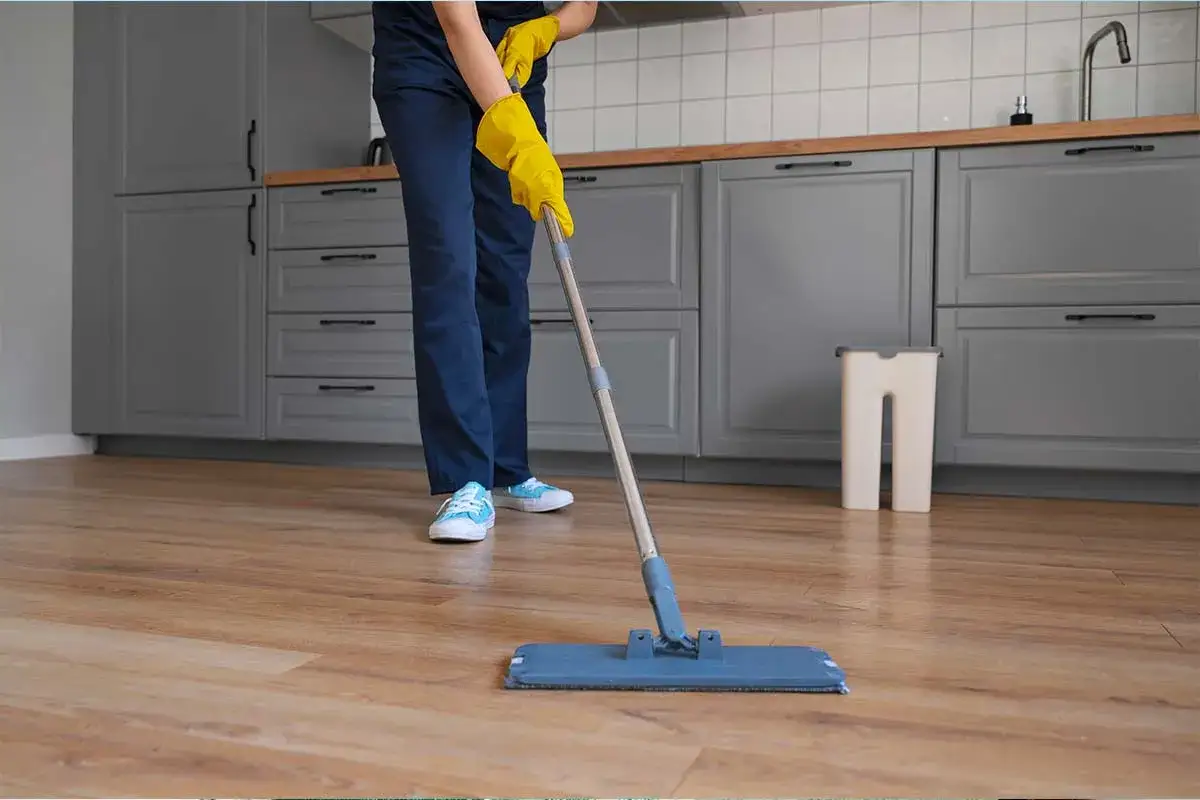 Persona con guanti gialli pulisce il pavimento in legno con uno straccio, usando un prodotto per pavimenti a base di ammoniaca per una pulizia profonda.