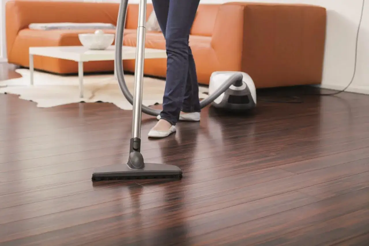 Pulizia parquet verniciato: una persona aspira il pavimento scuro, mantenendo la casa splendente.