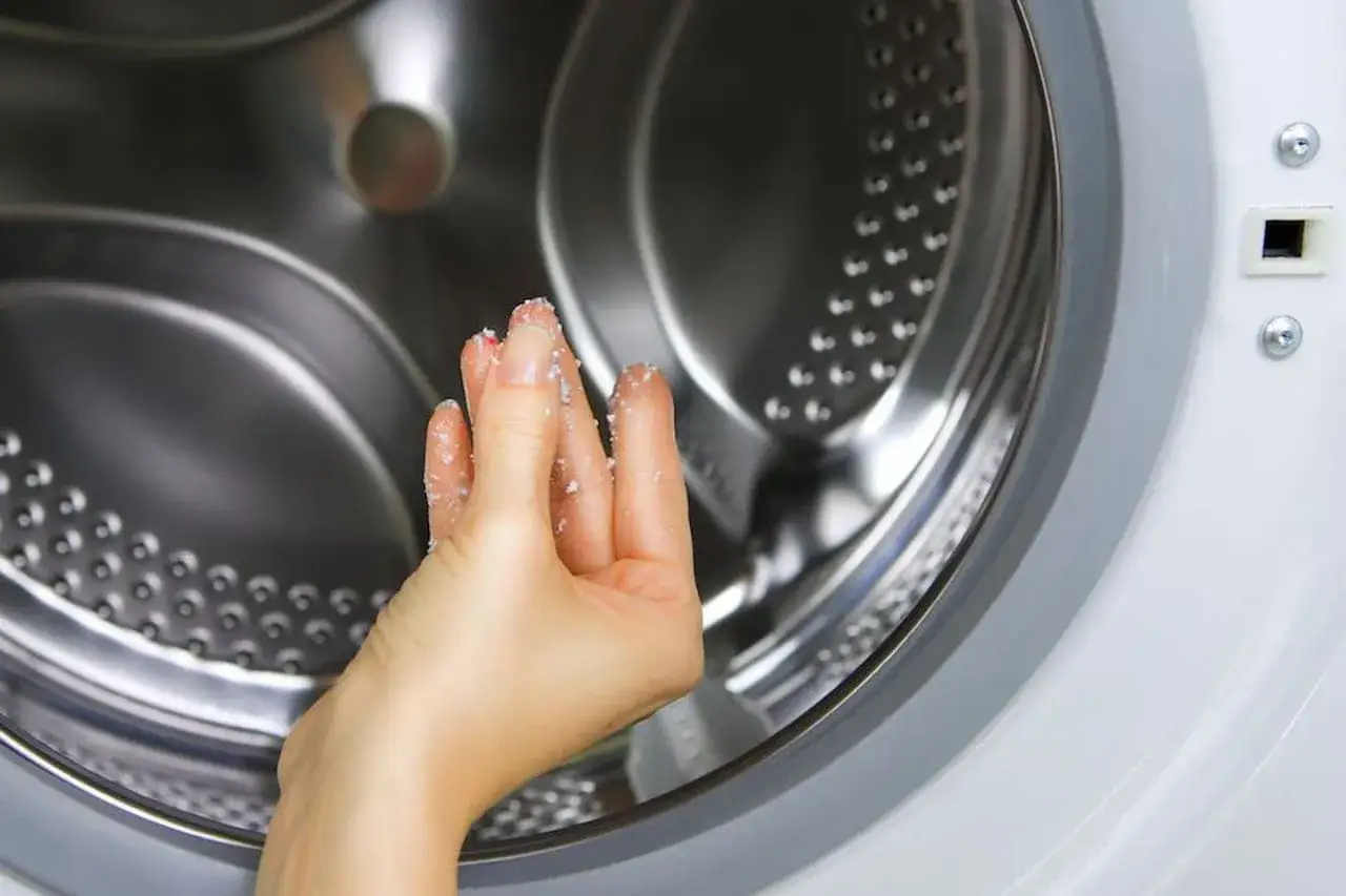 Mano con residui di bicarbonato e aceto, pronta a disinfettare la lavatrice per un bucato fresco e pulito.