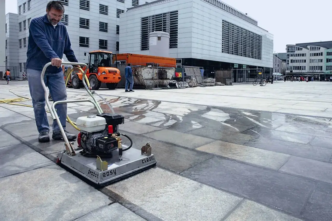 Uomo pulisce autobloccanti con idropulitrice in una piazza.