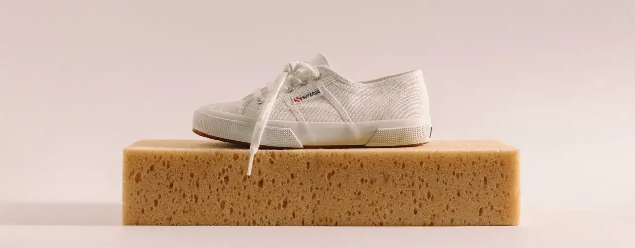 Una Superga bianca su una spugna gialla, pronta per essere lavata in lavatrice.
