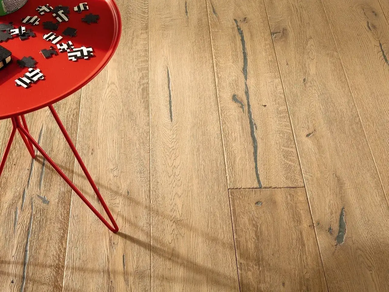 Un tavolino rosso con pezzi di puzzle su un pavimento in parquet. Scopri come si lava il parquet per mantenerlo splendente.