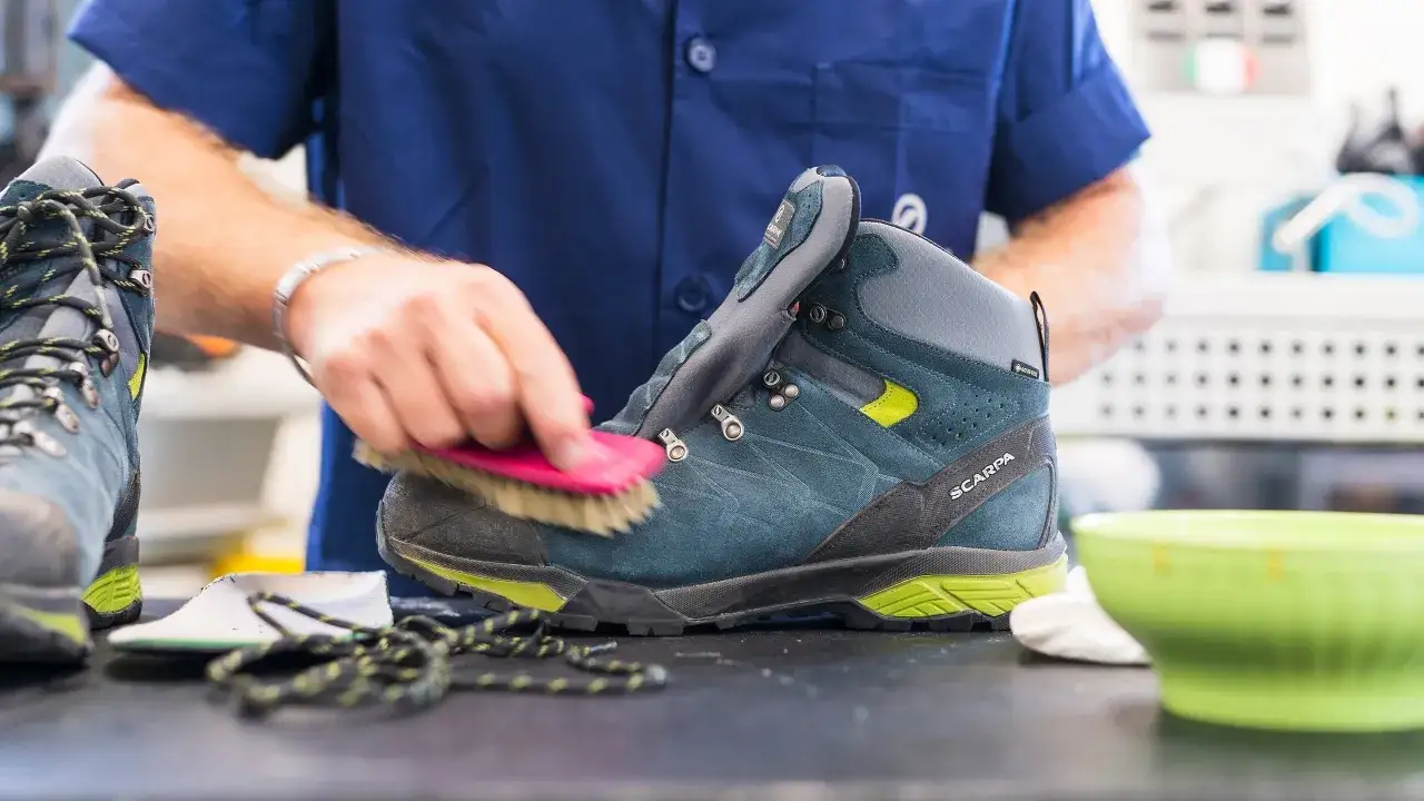 Mani che puliscono scarponi da trekking con una spazzola, un passo fondamentale per sapere come lavare le scarpe da trekking in lavatrice.