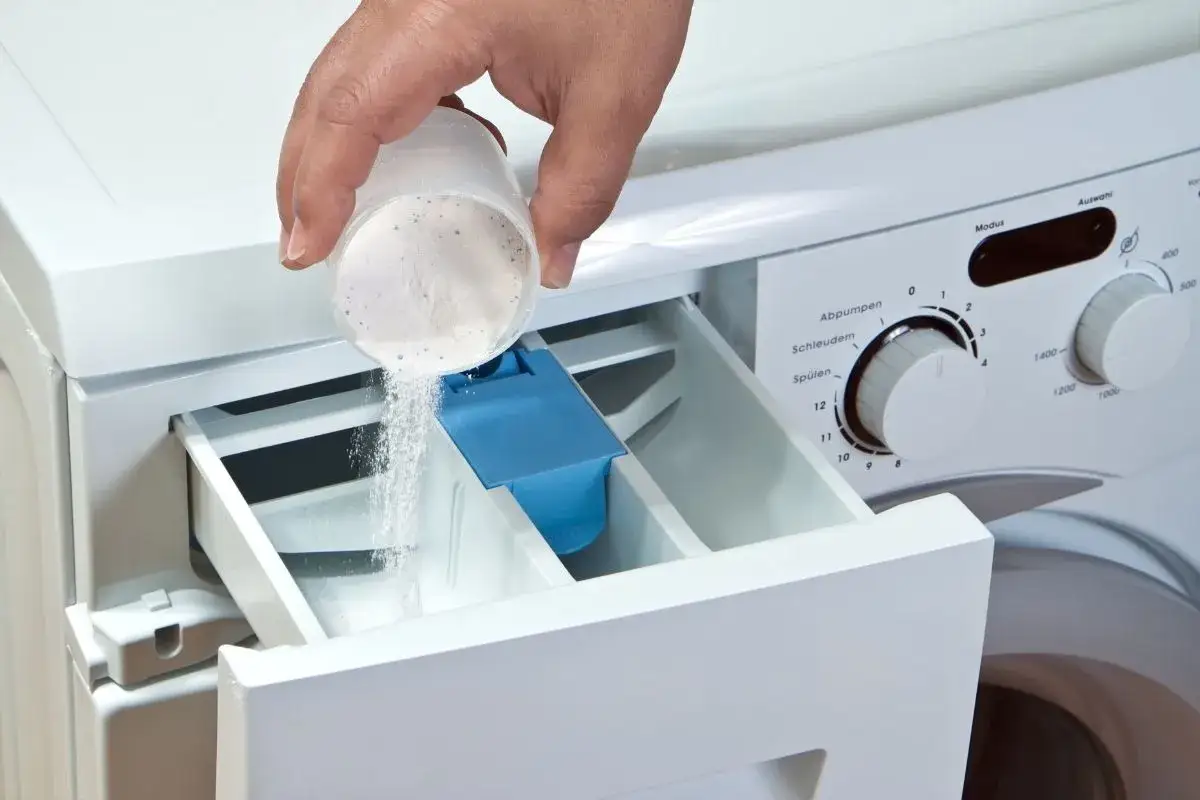Mano versa detersivo in polvere nel cassetto della lavatrice. Attenzione, troppo detersivo in polvere rovina lavatrice!