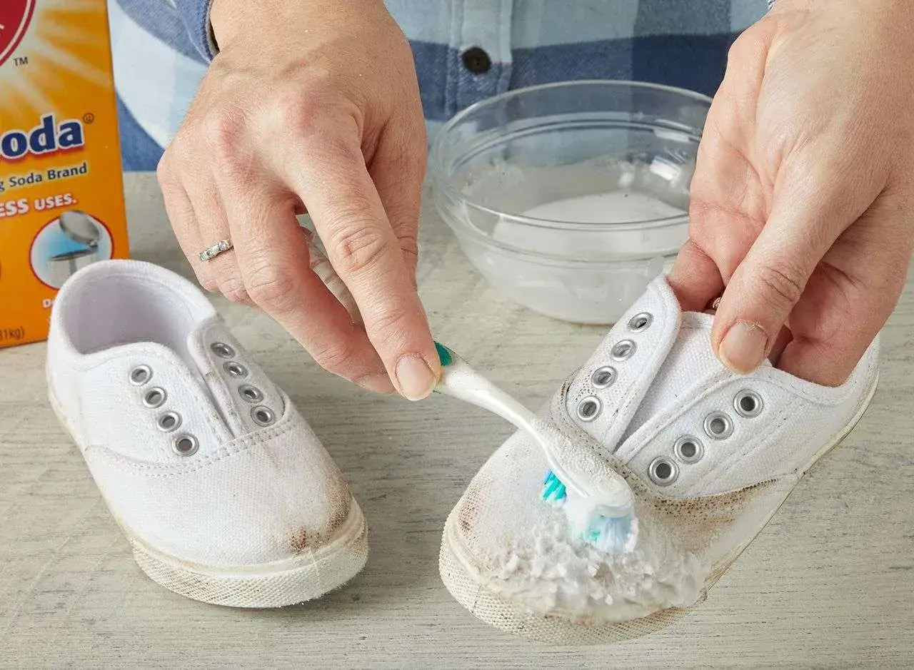 Mani che puliscono scarpe bianche sporche con uno spazzolino e bicarbonato, per farle tornare come nuove.