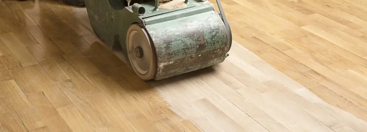 Macchina levigatrice in azione per come lucidare parquet, rivelando il legno chiaro sotto la vecchia finitura.