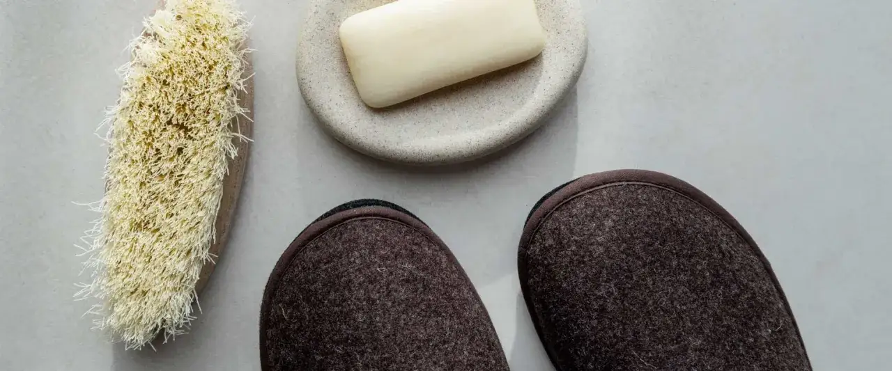Spazzola, sapone e pantofole marroni, pronti per scoprire come lavare pantofole in lavatrice per farle tornare come nuove.