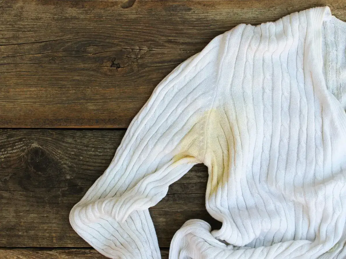 Maglione bianco con evidenti macchie gialle sotto l'ascella, segno che i vestiti nell'armadio necessitano di un lavaggio.