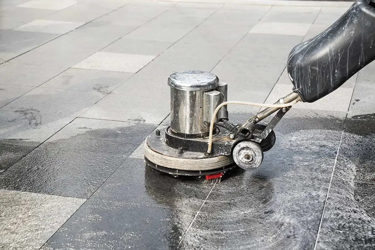Macchina per pulire pavimento esterno con acido muriatico, che lucida le lastre di pietra bagnate.
