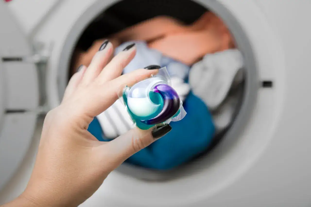 Mano con un detersivo in capsula per lavatrice, pronto per essere usato.