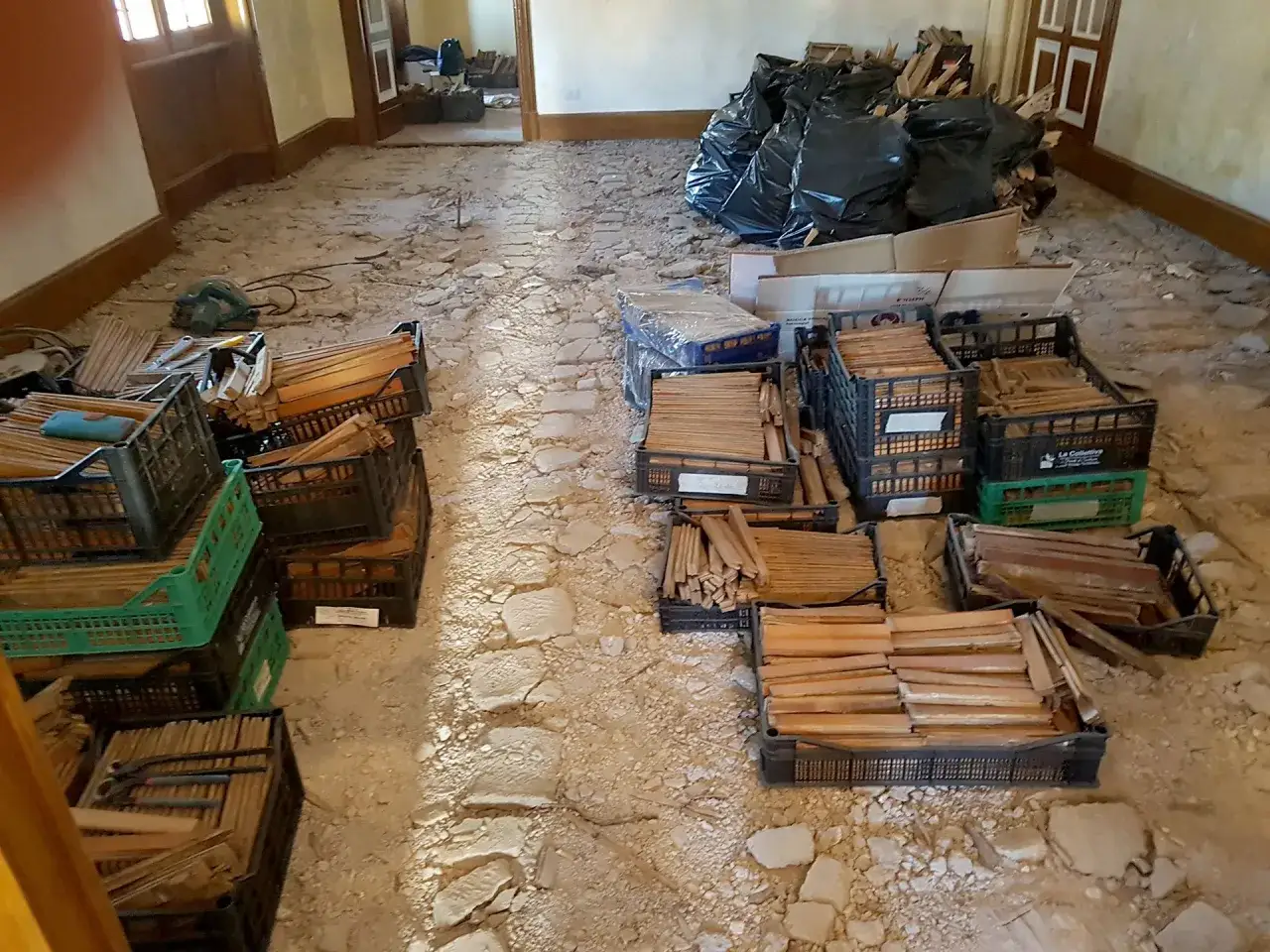 Rinnovare un parquet vecchio: assi di legno in cassette, sacchi neri e attrezzi pronti per il lavoro.