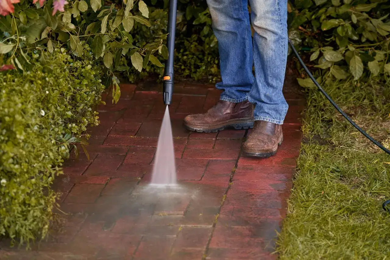 Uomo pulisce con idropulitrice un vialetto in pietra naturale esterna, mostrando come pulire la pietra naturale esterna in modo efficace.