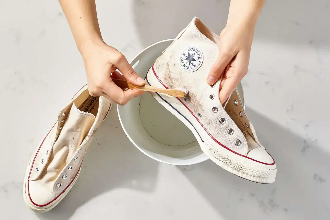 Mani che puliscono con uno spazzolino le Converse bianche macchiate, immerse in una bacinella. Ecco come lavare le all star bianche per farle tornare come nuove.