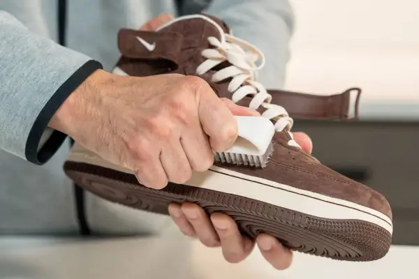 Mani che puliscono una scarpa di pelle scamosciata marrone con una spazzola, mostrando come pulire le scarpe di pelle.