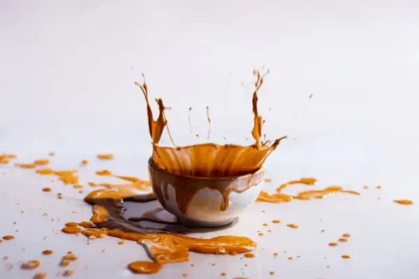 Un caffè schizza da una tazza, creando un'onda liquida. Le macchie di caffè vanno via, lasciando una scia dorata sulla superficie bianca.