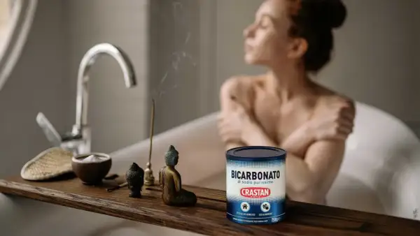 Una donna rilassata in vasca da bagno, con incenso e una ciotola di bicarbonato di sodio purissimo, un prodotto versatile per la casa e l'alimentazione.