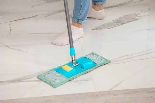 Piedi in calzini bianchi puliscono un pavimento in marmo con uno straccio blu e verde. Ecco come pulire il marmo per farlo brillare.