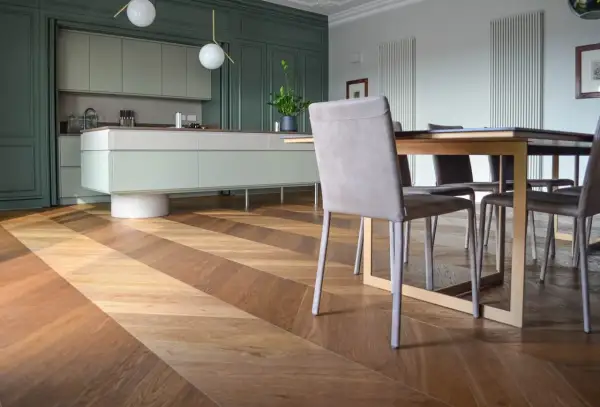 Un elegante parquet a spina di pesce in legno crea un motivo a zig-zag, che si estende dalla cucina moderna alla zona pranzo.