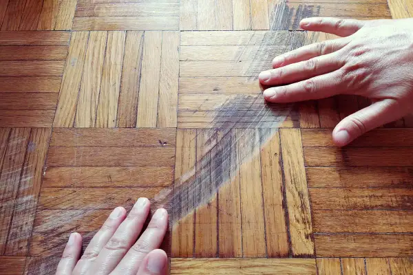 Mani sul parquet rovinato, graffi e segni evidenti. Si cerca una soluzione per pulire e ripristinare il legno.