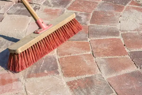 Una scopa con setole rosse su sanpietrini rossi e sabbia. Un modo semplice per capire come pulire i sanpietrini.