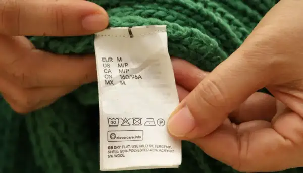 Etichetta di un maglione verde: non usare candeggina su poliestere. Asciugare in piano, usare un detergente delicato.