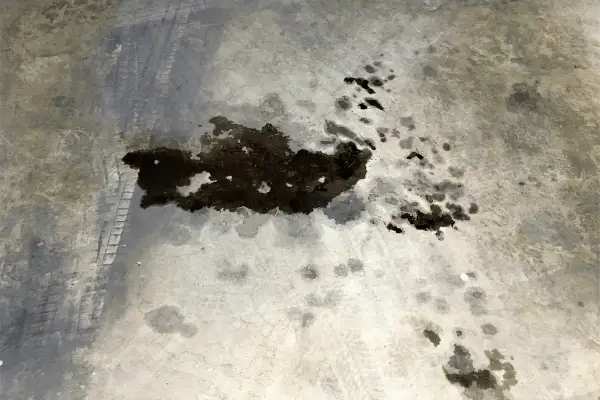 Macchie scure di grasso meccanico sul cemento, con tracce di pneumatici. Un problema comune da risolvere per chi lavora con i motori.