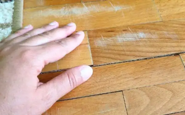 Mano sul parquet con macchie vecchie di olio e graffi evidenti.